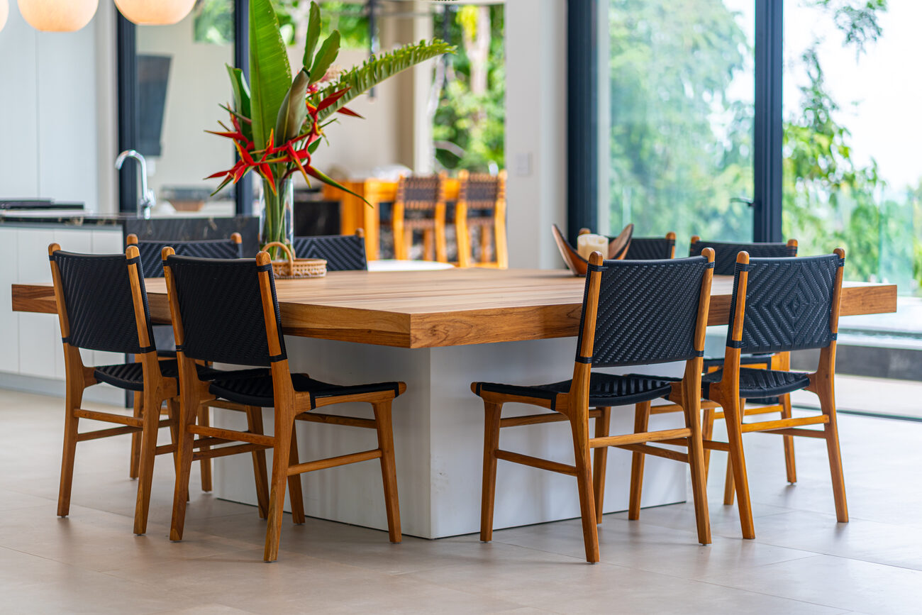 The teak dining table and woven chairs, with the garden beyond the glass