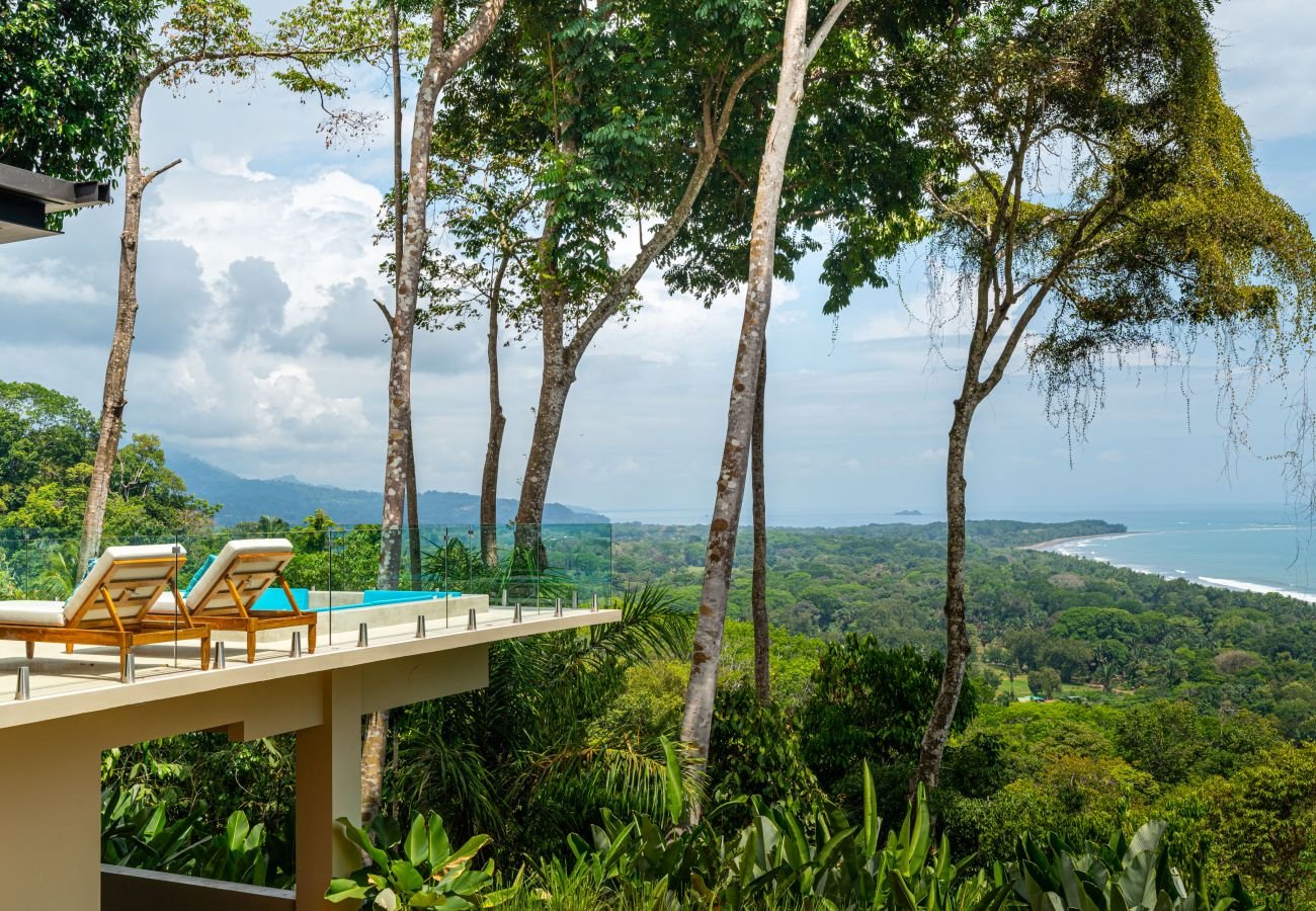 The open dining and kitchen — square teak table, marble island, double-height volume